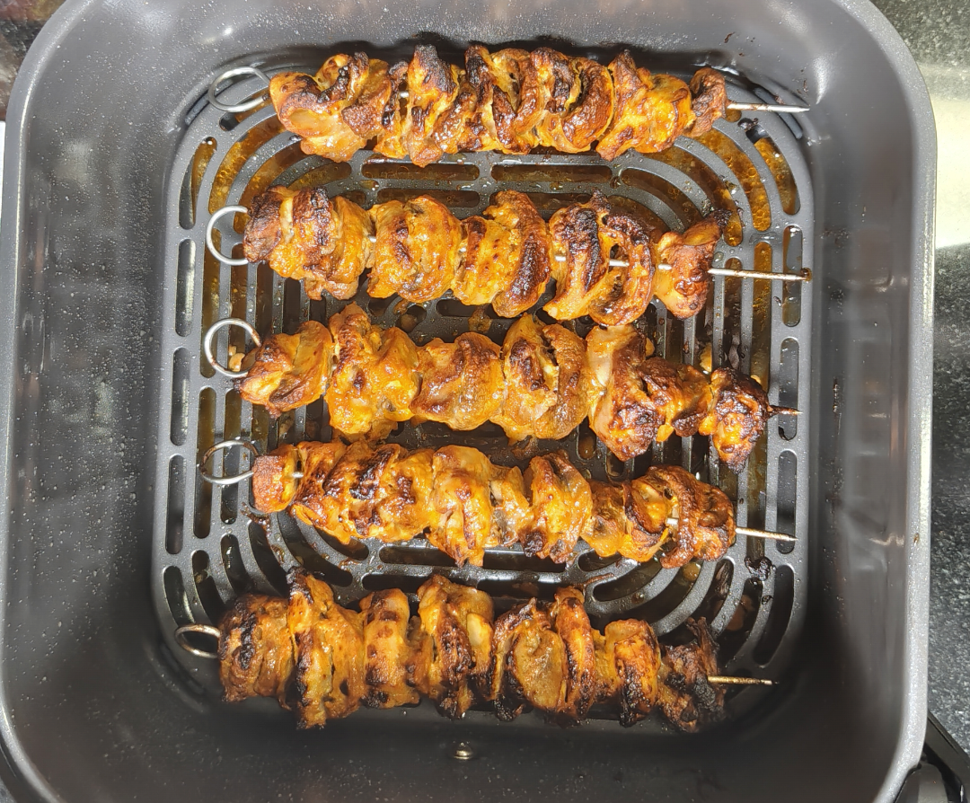 Five cooked chicken tikka and mushroom skewers with browned edges inside the air fryer basket