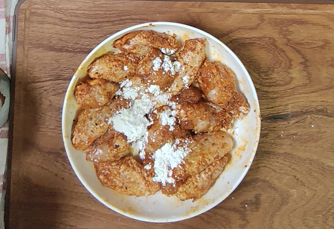 Corn starch sprinkled over the seasoned chicken wings in the bowl