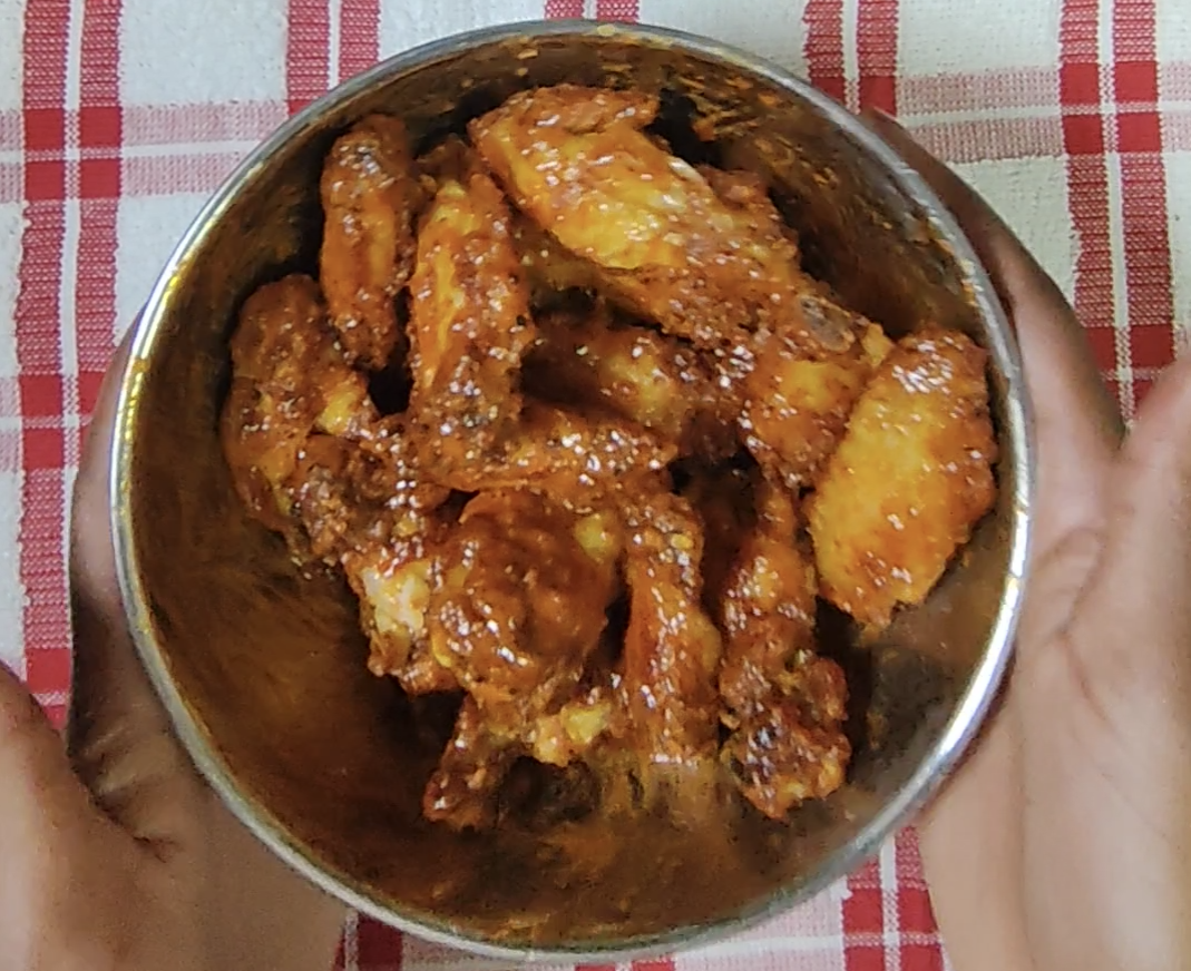 Sticky Sriracha-coated chicken wings glistening in the mixing bowl after tossing