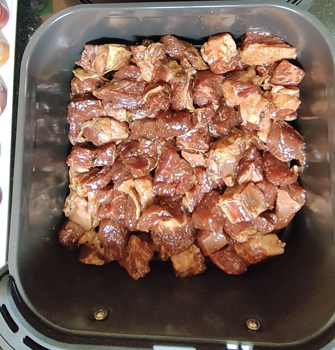 Raw seasoned beef cubes arranged on the crisper plate in an air fryer basket