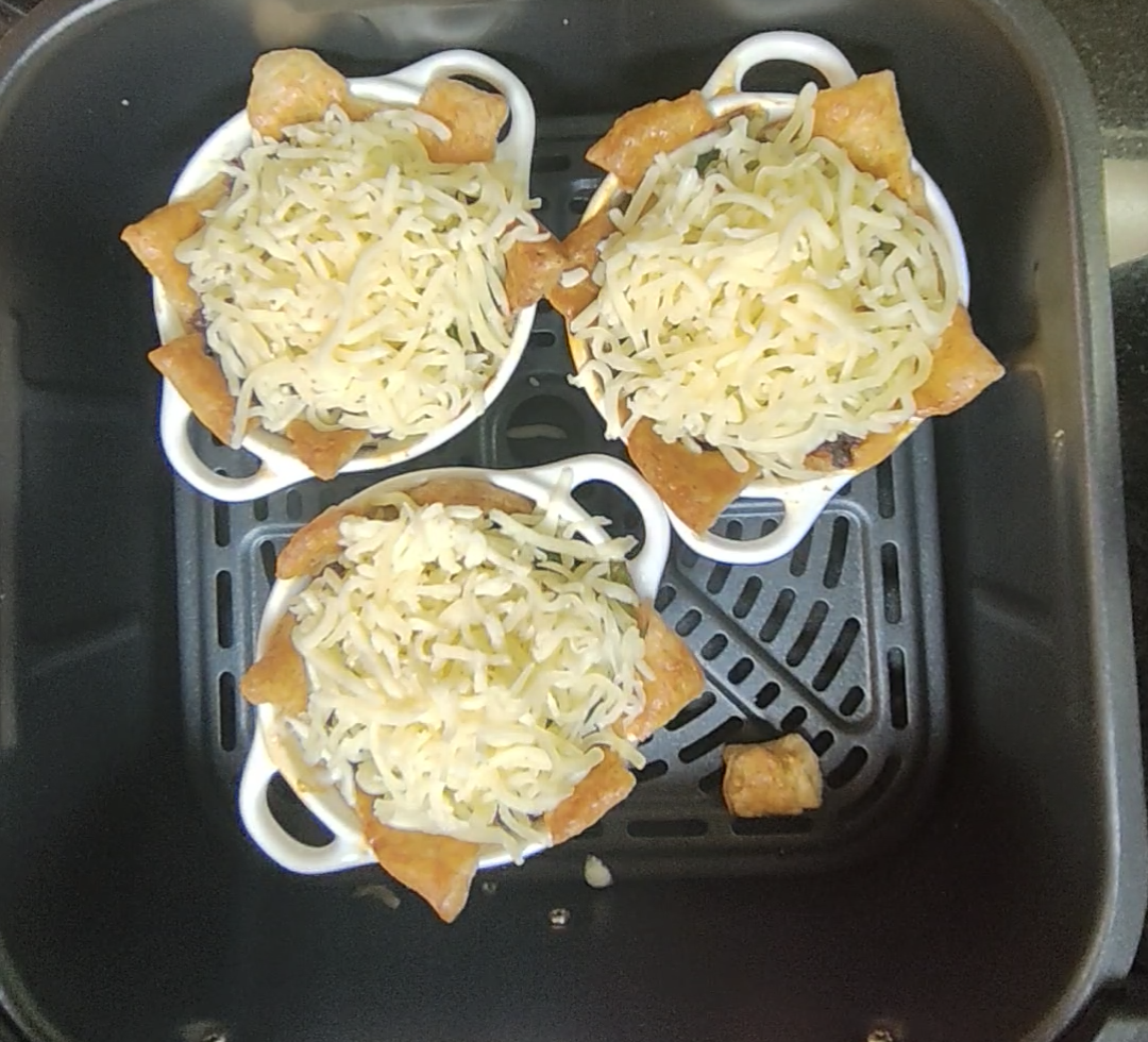 Three pastry pots covered with shredded mozzarella in the air fryer basket before the second cooking stage