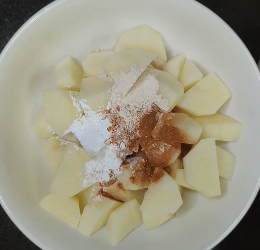 Potato chunks of similar size in a white bowl with seasoning sprinkled on top, before air frying