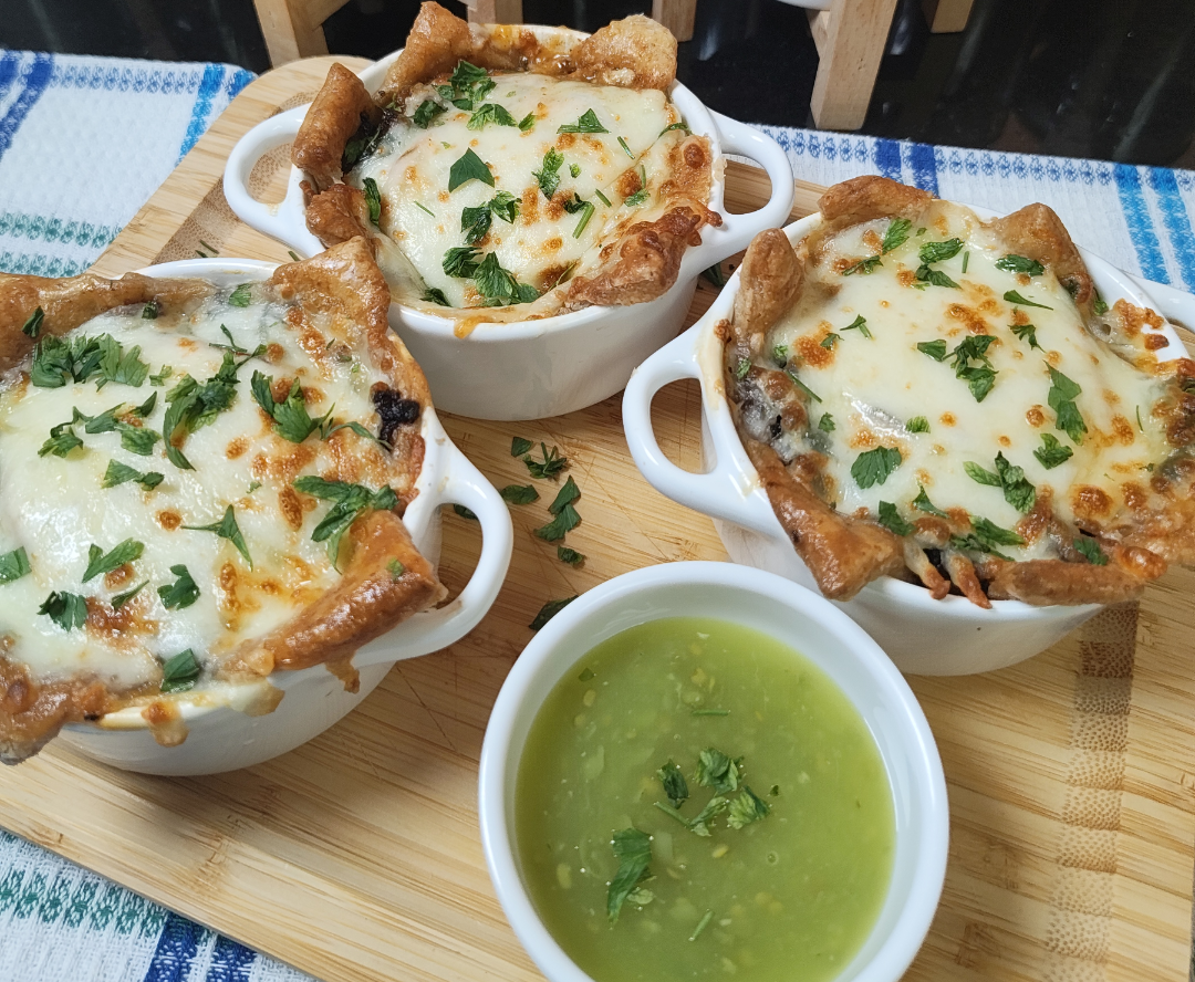 Close-up of finished beef and cheese pastry pots with melted mozzarella, coriander and crisp pastry edges beside green chilli sauce
