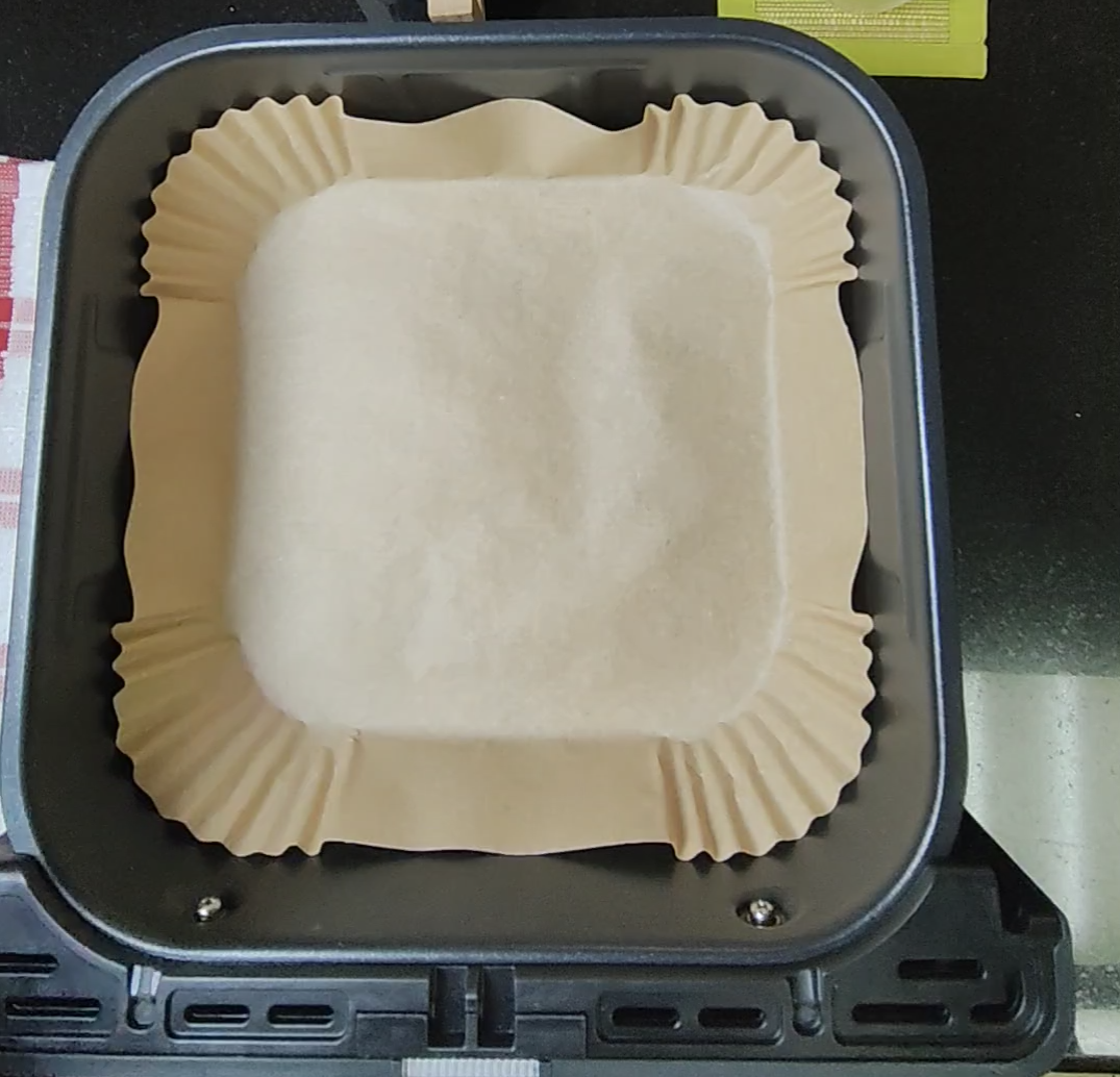 Empty parchment-style liner resting in an air fryer basket with the appliance switched off