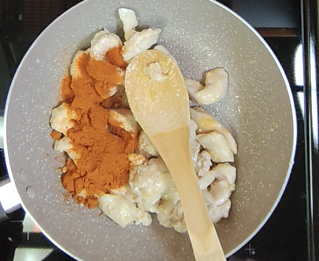 Chicken fajita seasoning added over the chicken strips in the frying pan