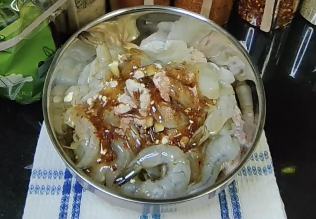 Cleaned shrimp in a metal mixing bowl with the seasonings and avocado oil added