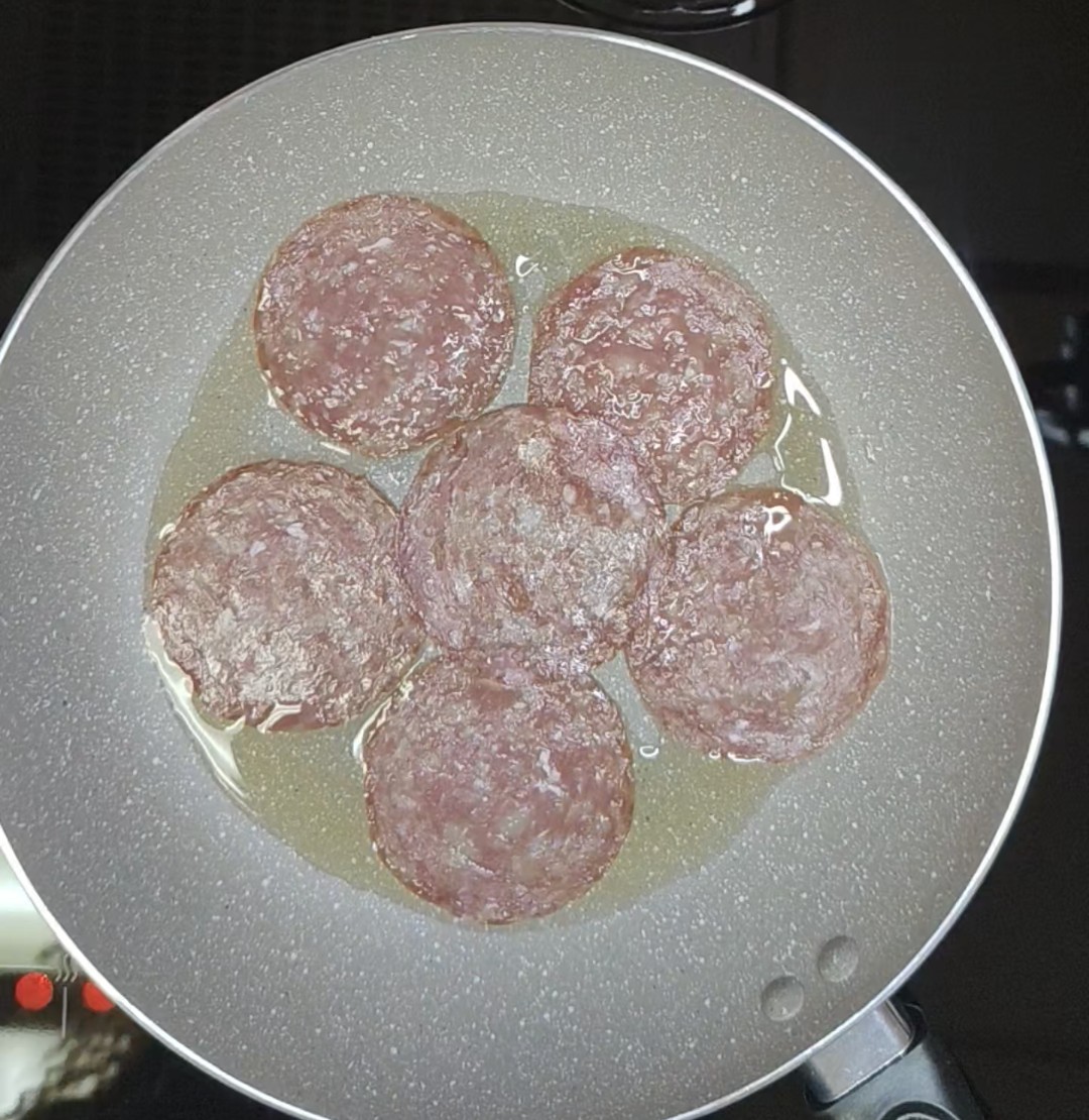 Six salami slices arranged in a frying pan with avocado oil