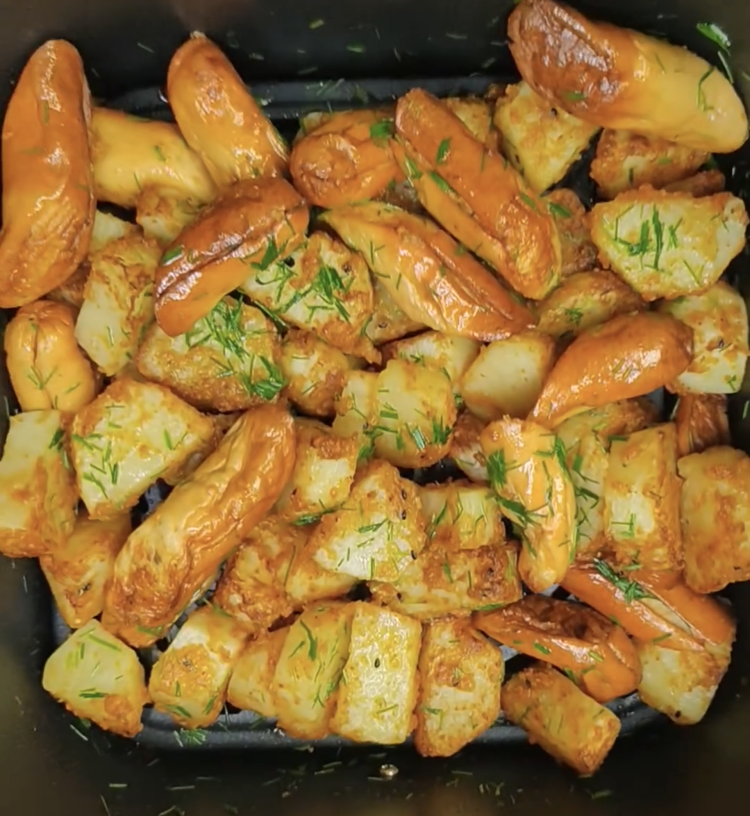 Cooked potatoes and chicken sausages garnished with chopped chives in the air fryer basket