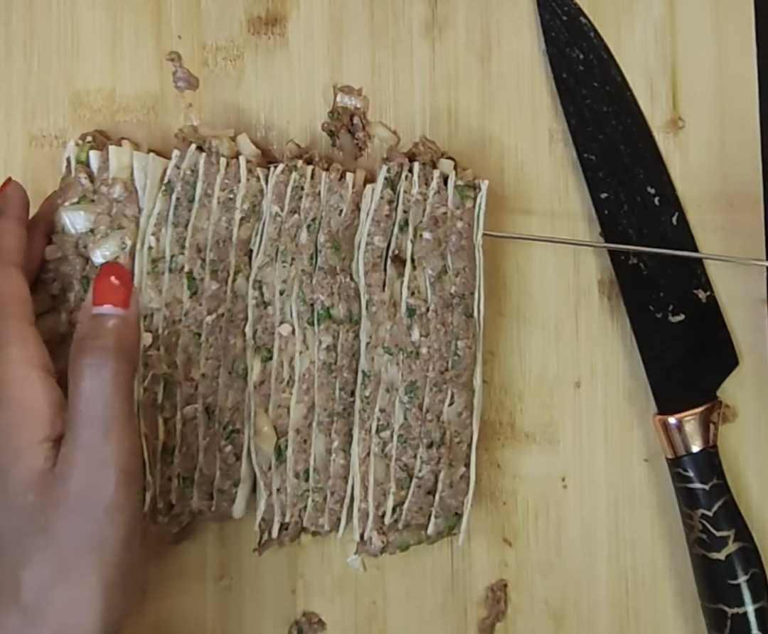 Stacked tortilla and beef layers being cut and assembled onto a skewer