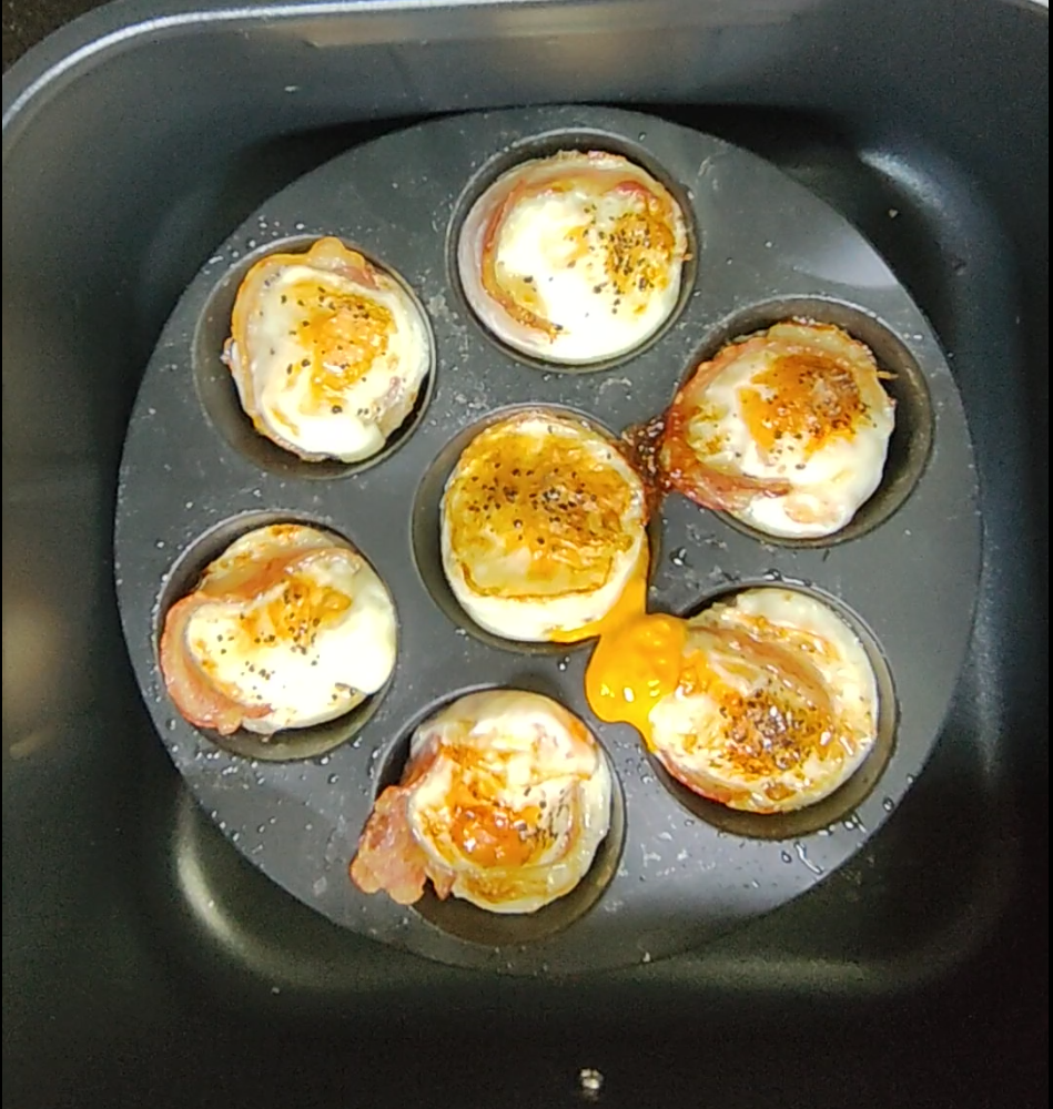 Cooked bacon and eggs seasoned with black pepper in a silicone mould inside an air fryer