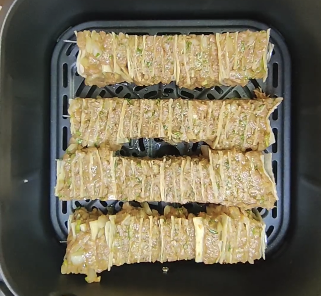 Four uncooked beef and tortilla skewers arranged in the air fryer basket