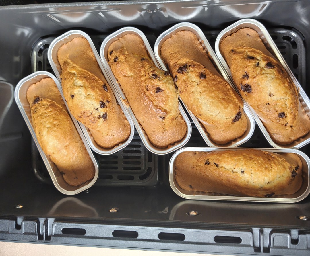 Close-up of golden mini chocolate chip cakes risen above their aluminium tins