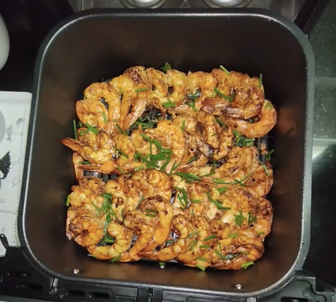 Cooked golden shrimp in the air fryer basket, garnished with chopped chives