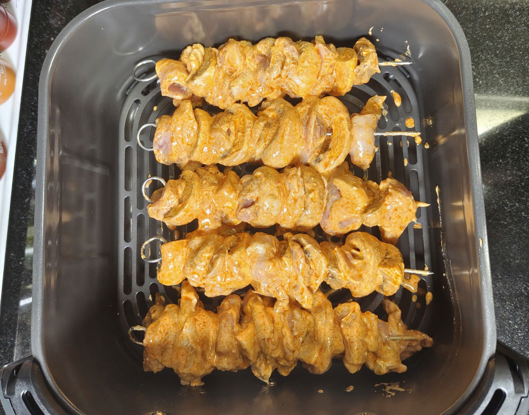 Raw marinated chicken tikka skewers arranged in the air fryer basket before cooking