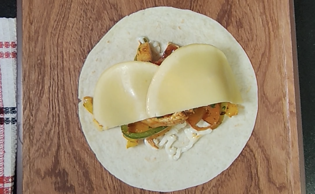 Two slices of mozzarella laid over the chicken fajita filling on a tortilla