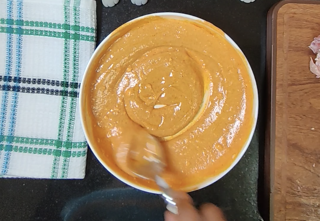 Creamy orange tikka marinade being stirred in a white bowl