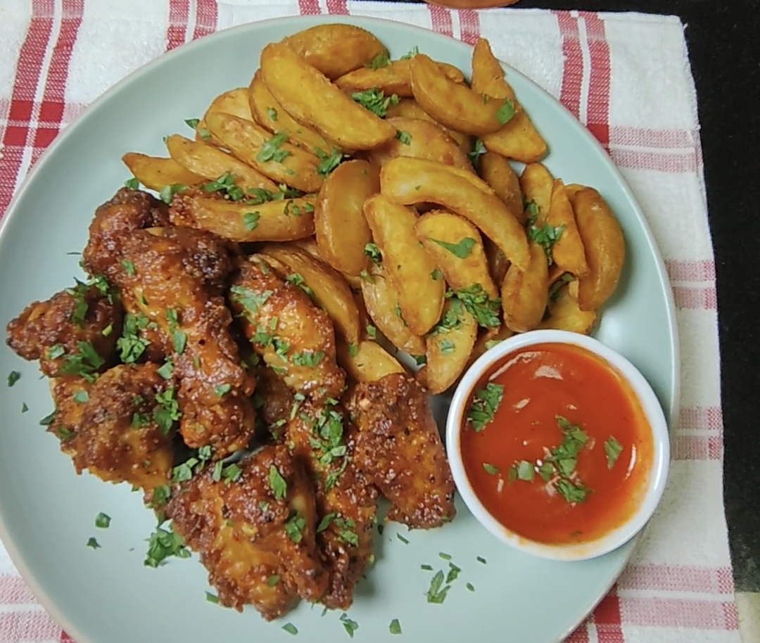 Overhead view of the finished sticky Sriracha chicken wings with golden potato wedges and a small dish of sauce on a pale blue plate