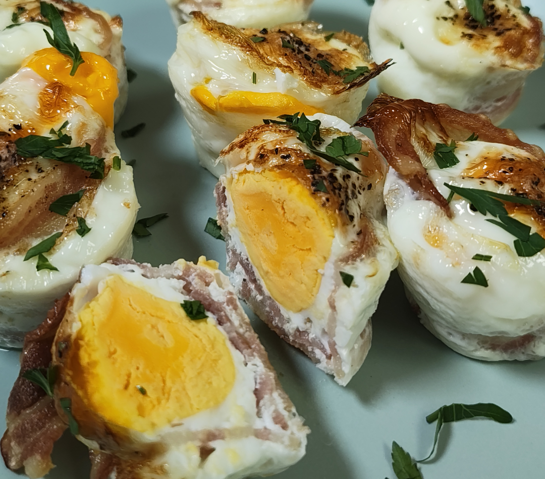 Air fryer bacon and egg cups on a plate, one cut open to show a firm yolk