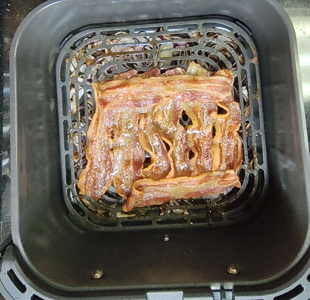 Golden crispy cooked bacon rashers on the air fryer crisper plate with softened onions underneath