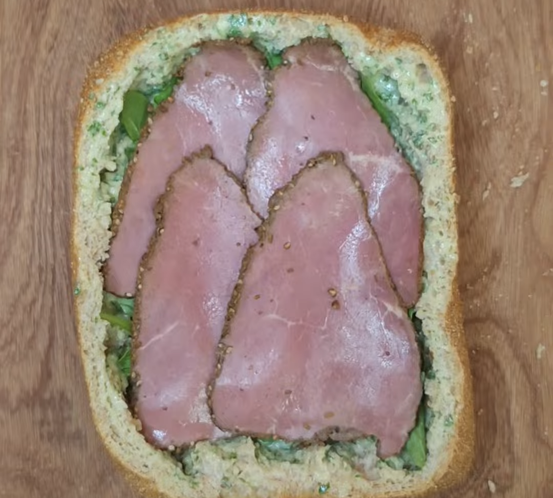 Four slices of pastrami layered inside country bread with baby spinach