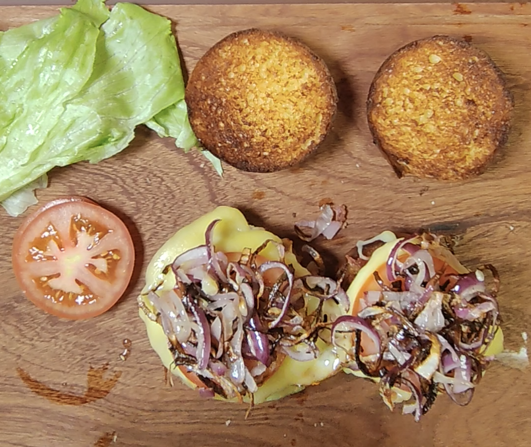 Bottom bun halves layered with bacon, cheesy fried eggs and cooked red onions during assembly