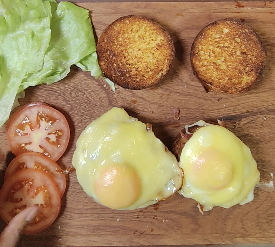 Butter toasted bun halves and two fried eggs topped with melted cheddar on a wooden board