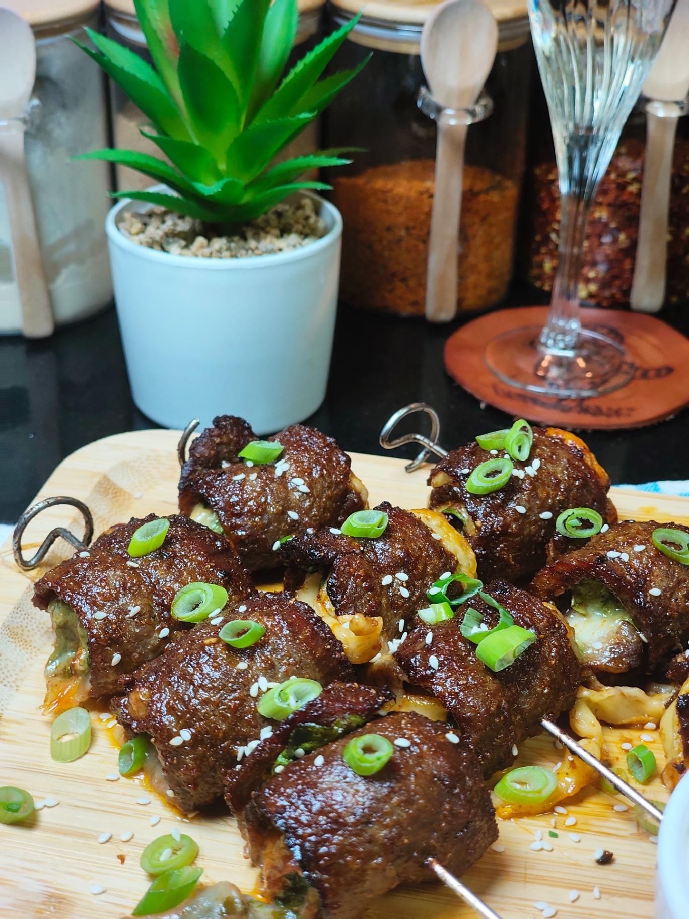 Finished browned beef rolls on metal skewers with melted cheese, sesame seeds and sliced spring onions