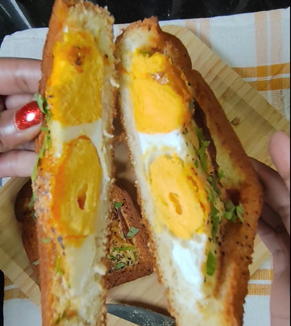 Hands holding two halves of an egg in a hole cut open to show firm yolks inside the toasted brioche