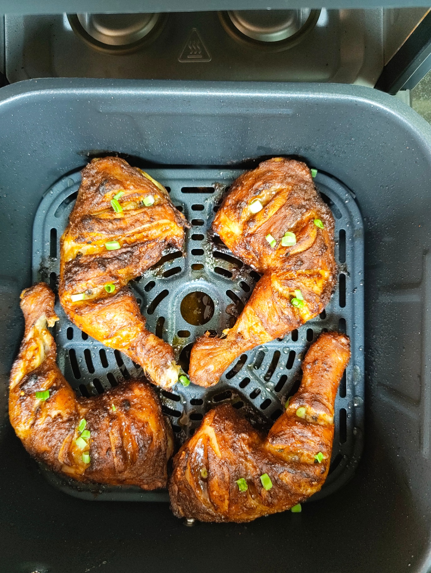 Four browned roasted chicken leg quarters sprinkled with chopped green onions in an air fryer basket