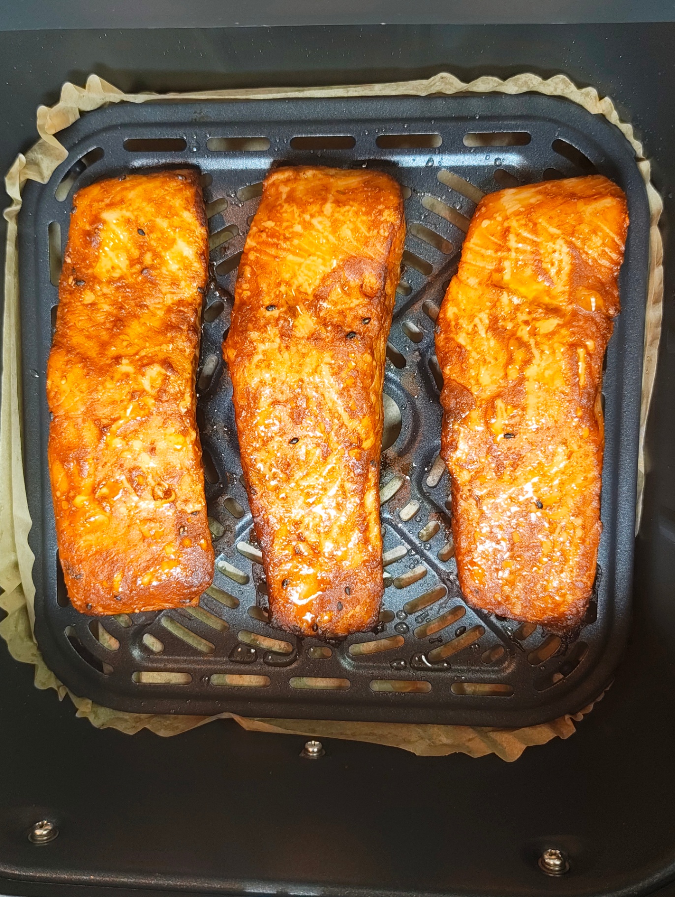 Three golden cooked salmon fillets in an air fryer basket
