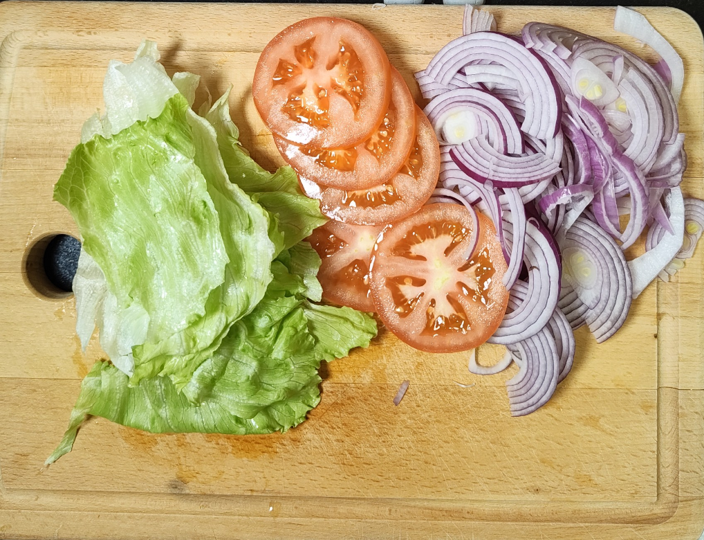 Fresh lettuce leaves, tomato slices and sliced red onion on a wooden chopping board