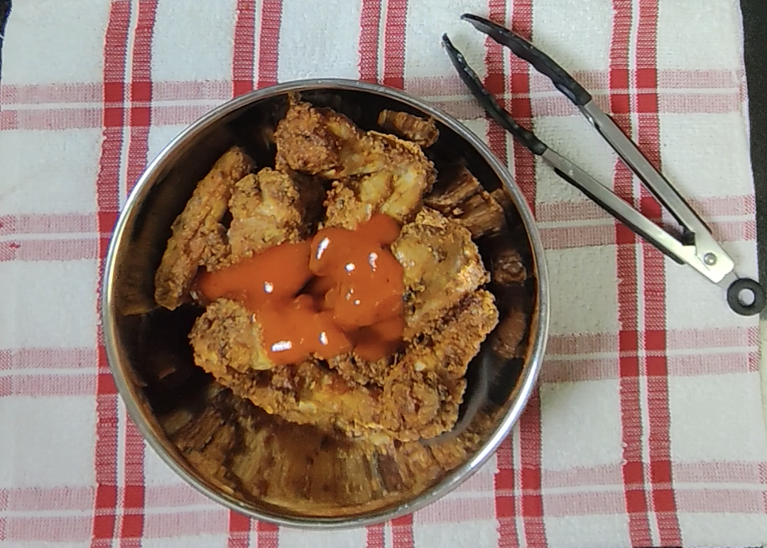 Warm Sriracha butter sauce poured over the cooked chicken wings in the mixing bowl