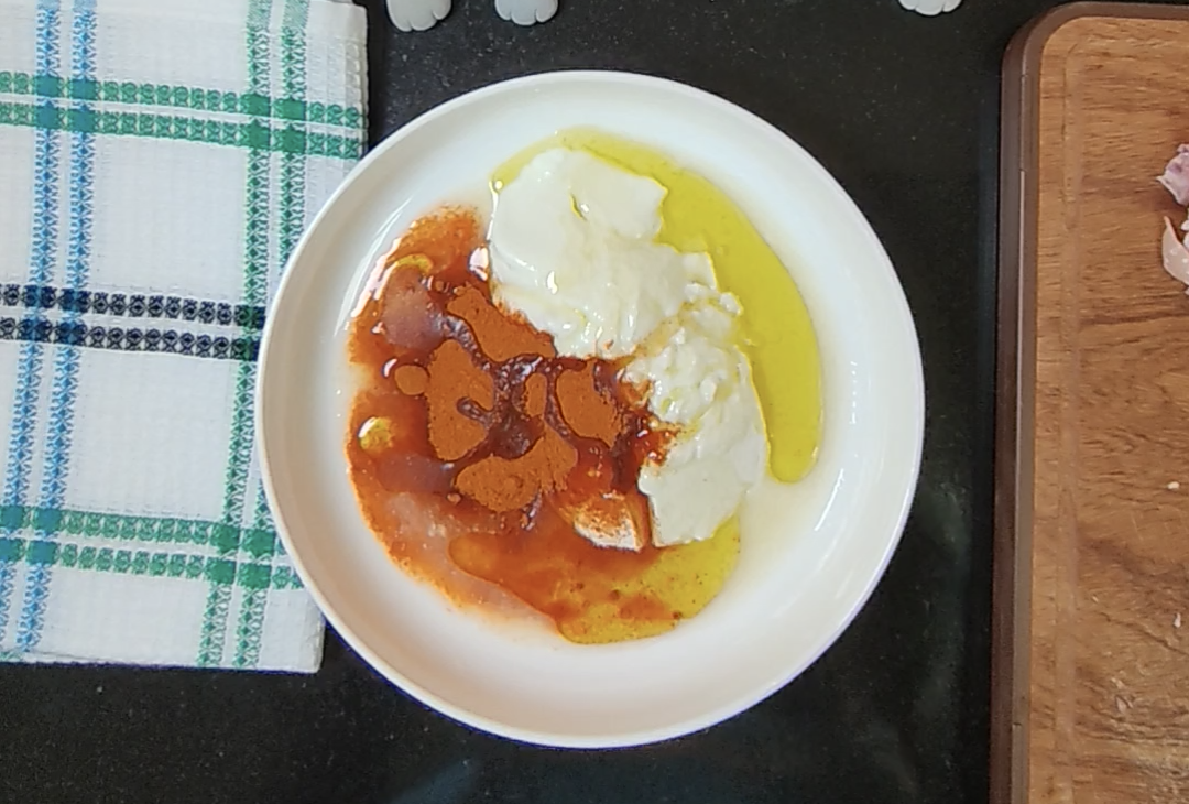 Natural yoghurt, tikka spice and olive oil in a white mixing bowl before combining the marinade