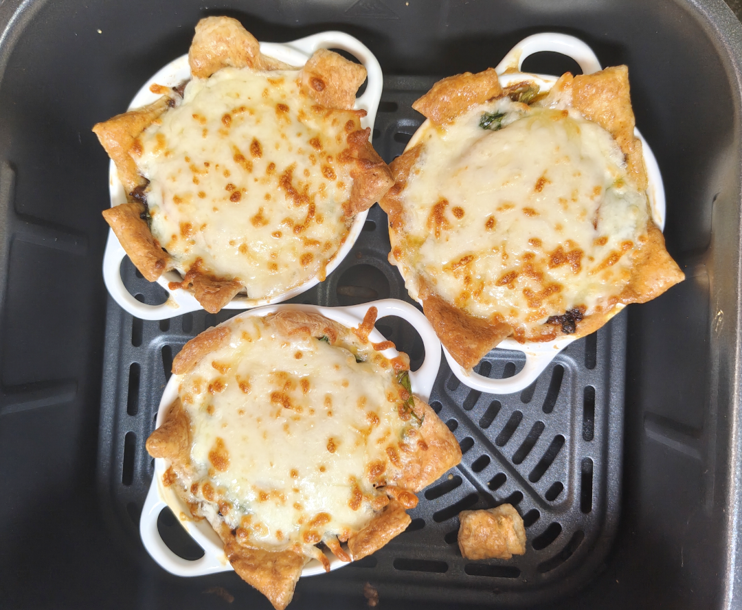 Three finished beef and cheese pastry pots with golden melted mozzarella inside the air fryer basket