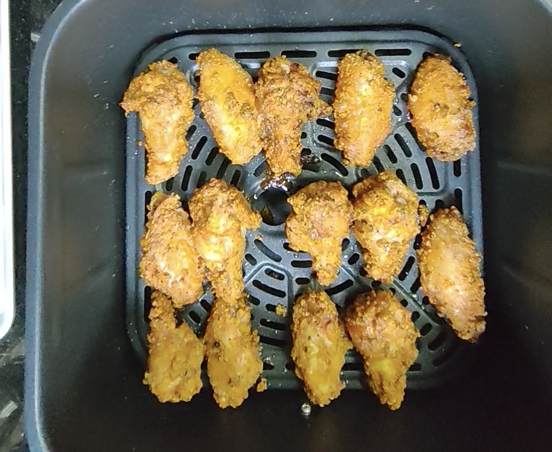 Golden cooked chicken wings inside the air fryer basket