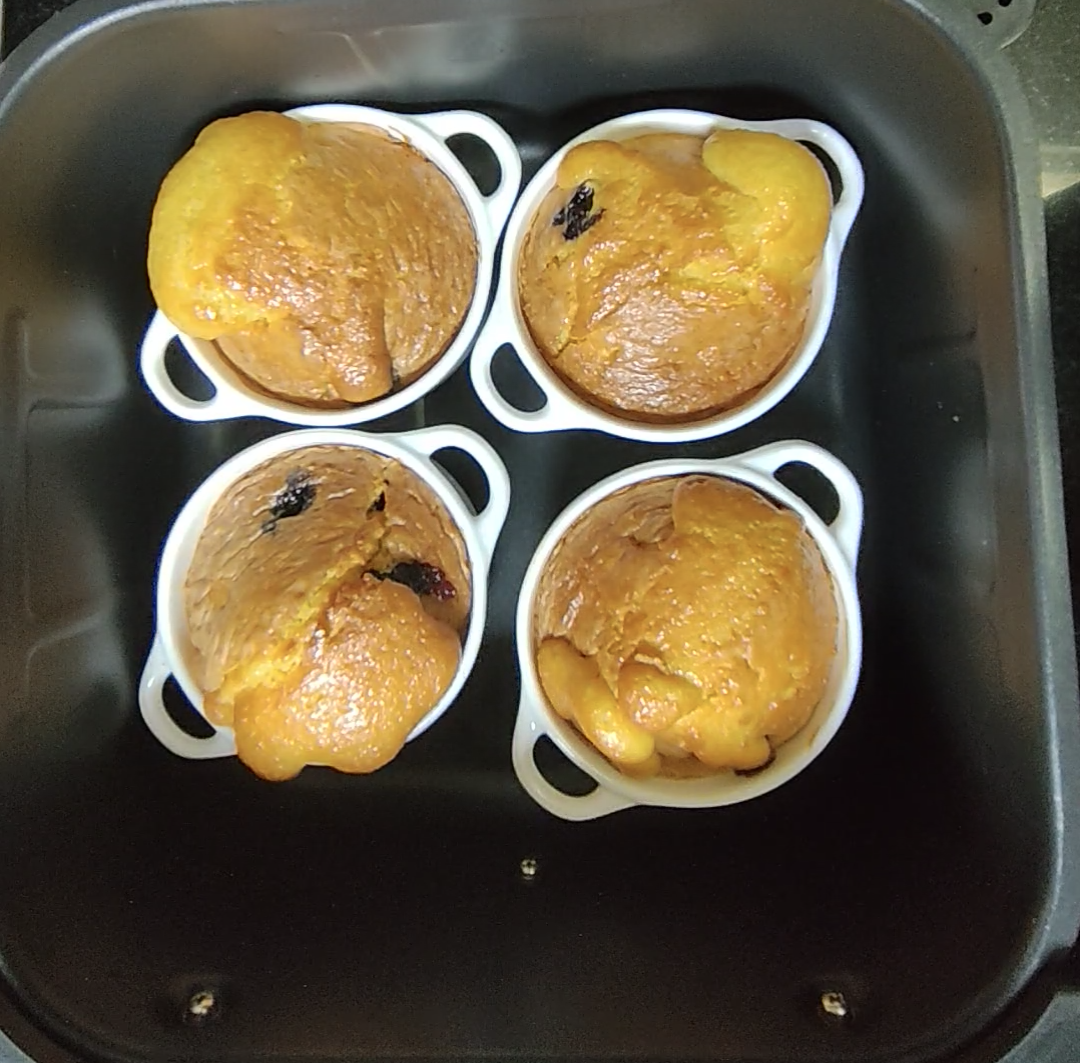 Four blueberry lemon muffins baked in white ceramic ramekins inside an air fryer basket