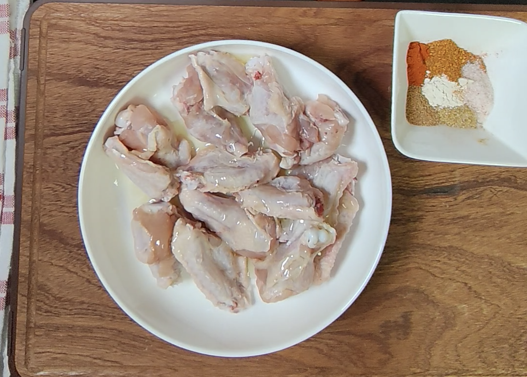 Raw chicken wings in a bowl with a small dish of dry seasonings beside them