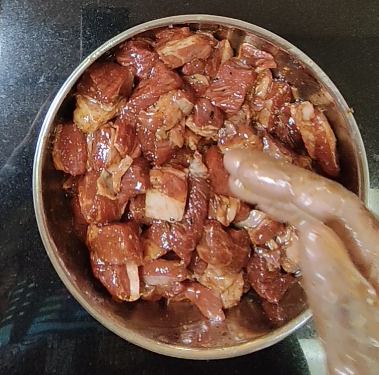Cubed steak coated in seasoning and sauces being mixed by hand in a metal bowl