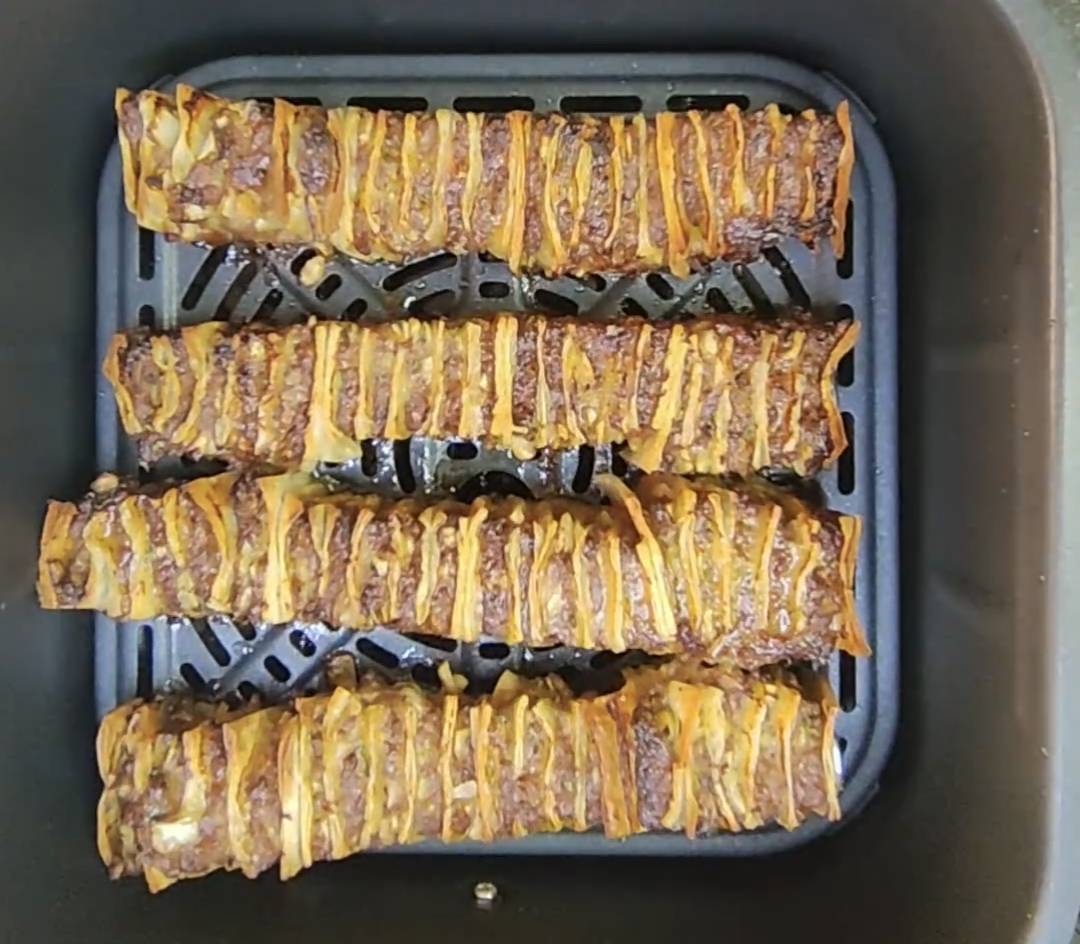 Four cooked beef and tortilla skewers, browned and golden in the air fryer basket