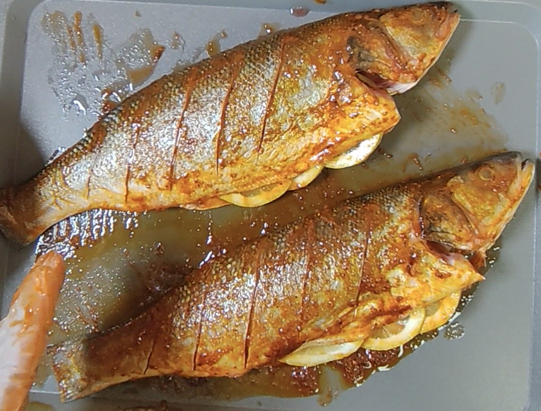 Two scored and seasoned whole sea bass with lemon slices in a roasting tray, before cooking