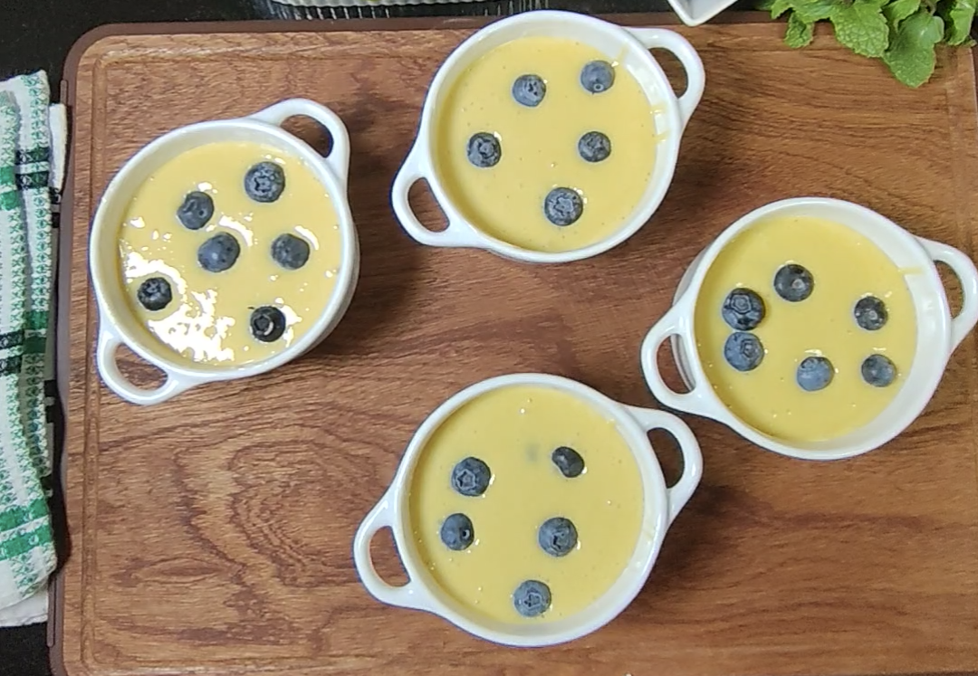 Lemon cake batter in four white ramekins, each topped with a few fresh blueberries