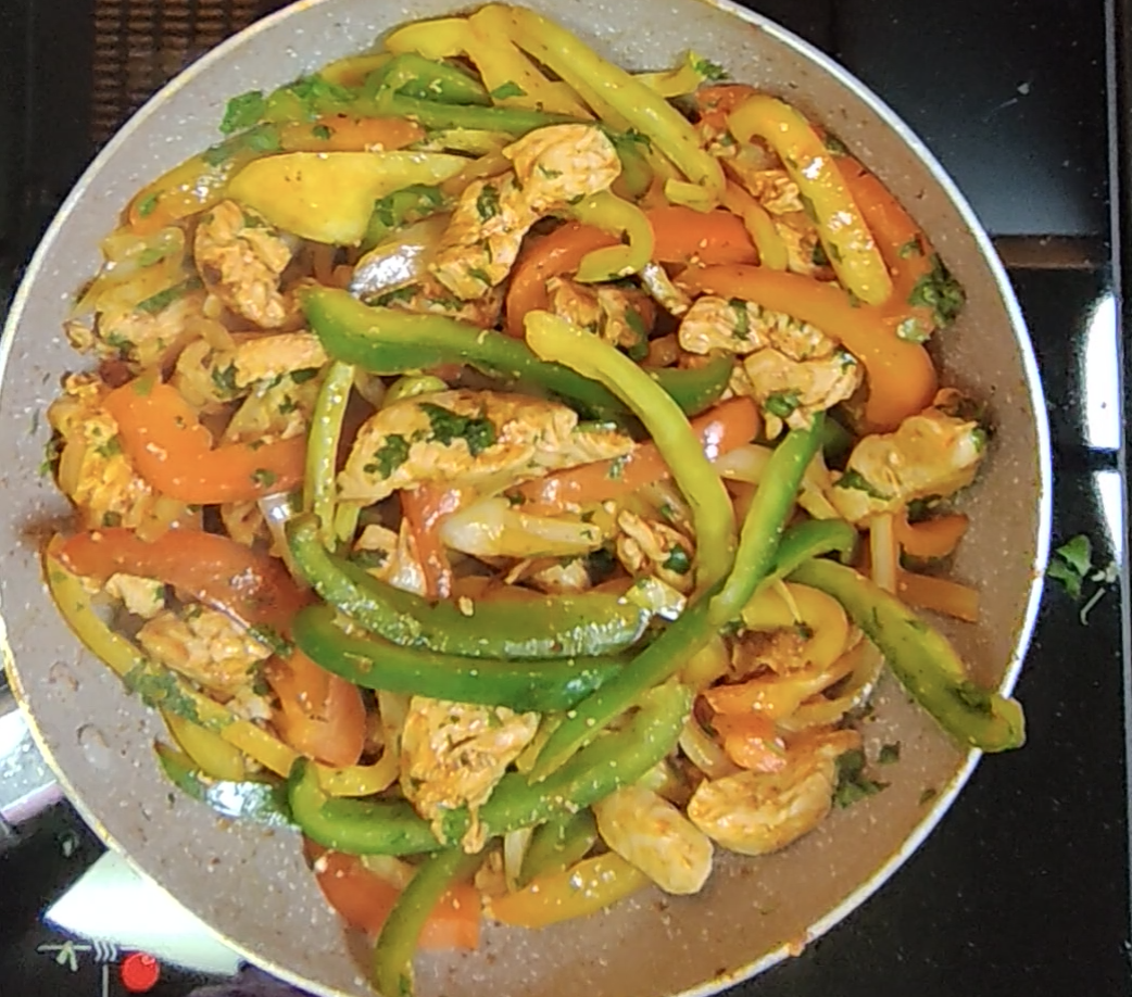 Finished chicken fajita filling with red, yellow and green peppers, onion and chopped coriander in the frying pan