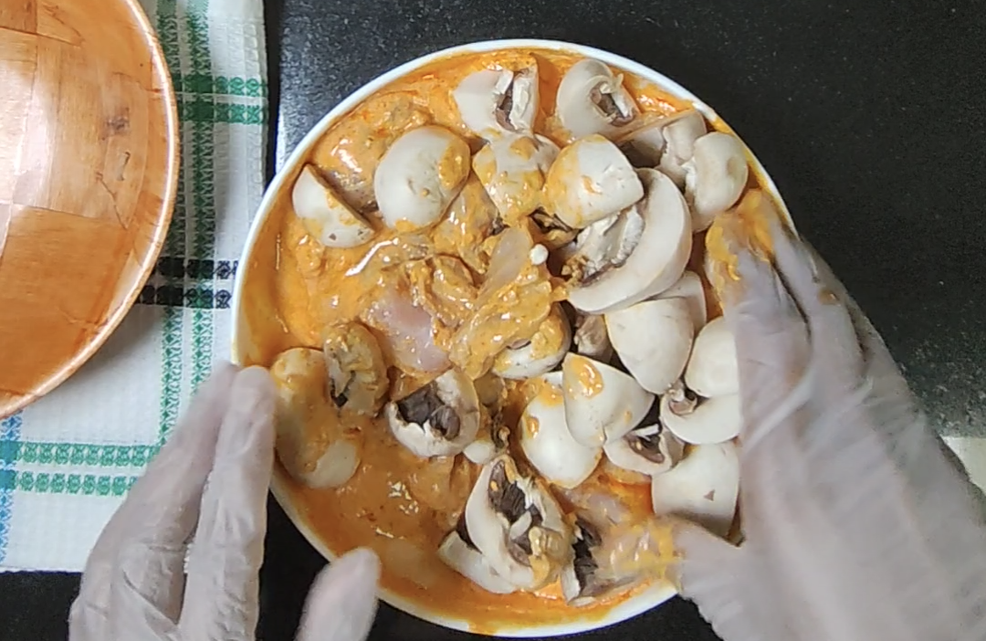 Prepared mushrooms being gently mixed into the chicken and orange tikka marinade
