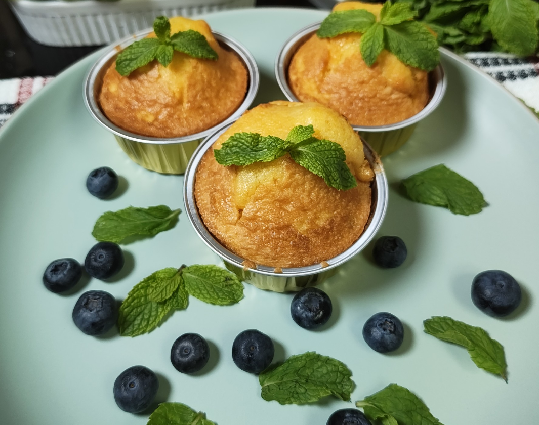 Three blueberry lemon muffins in disposable aluminium muffin cups on a pale blue plate with fresh mint and blueberries