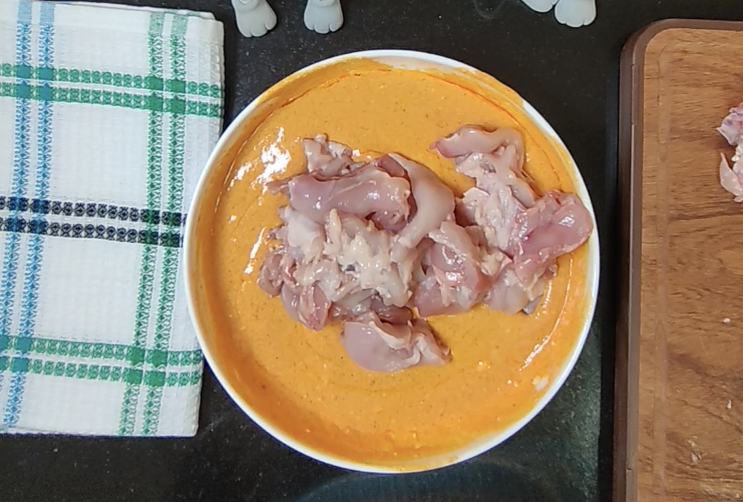 Raw boneless chicken thigh pieces added to the orange tikka marinade before coating