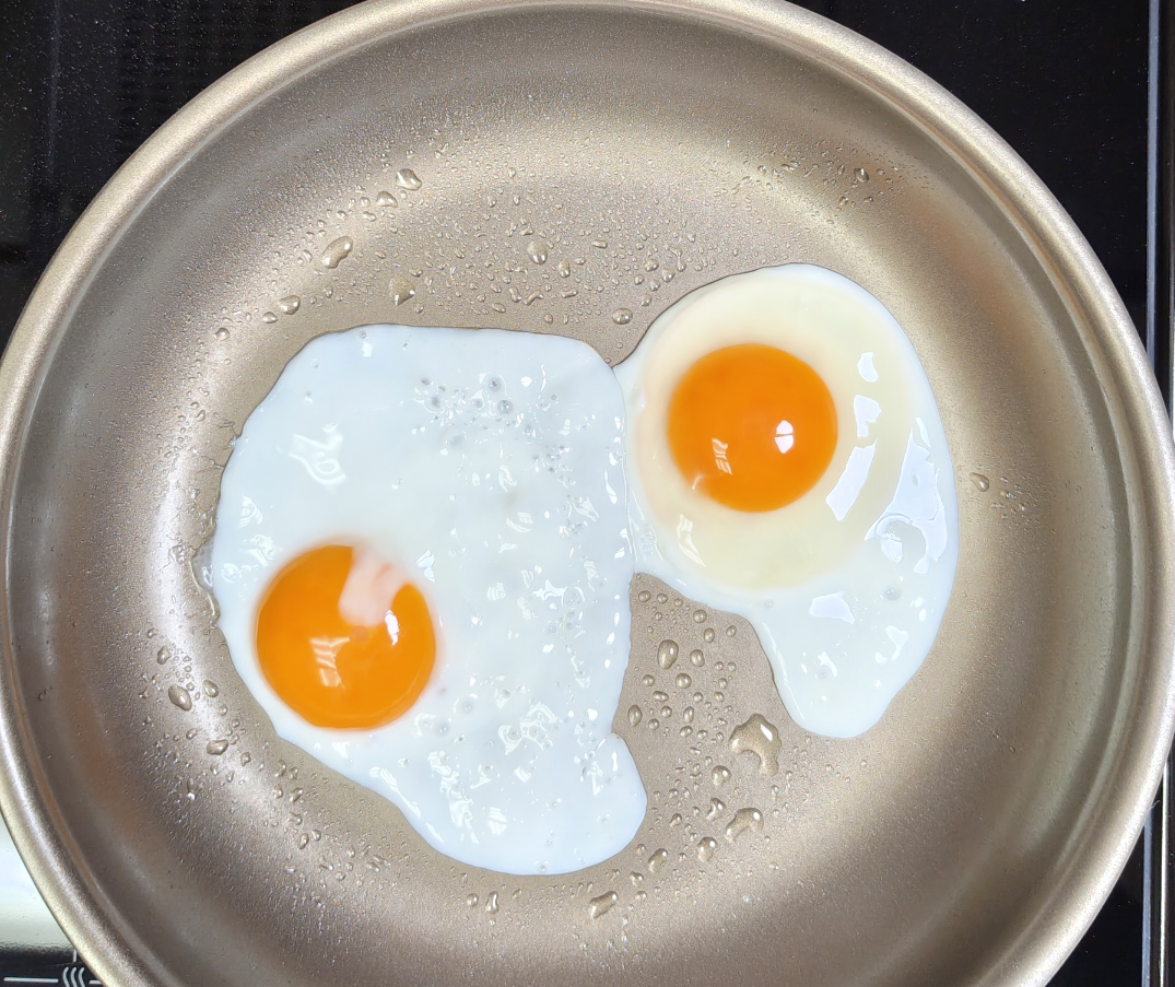 Two eggs frying in a pan with a little olive oil