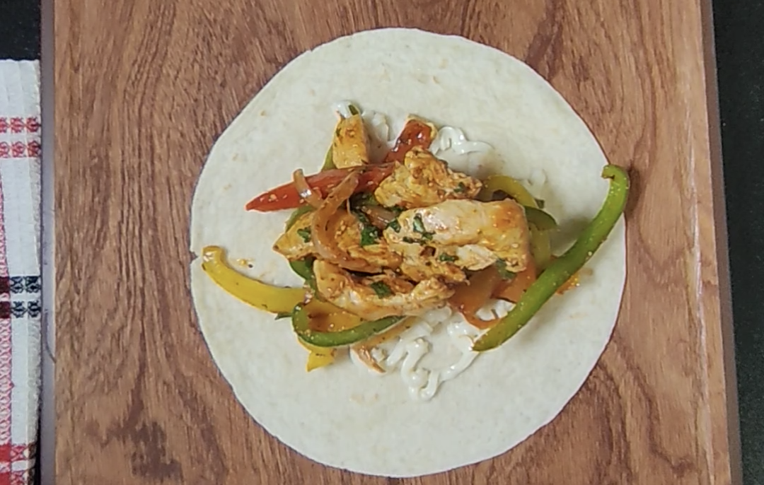 Chicken fajita filling spooned over mayonnaise on a tortilla on a wooden board