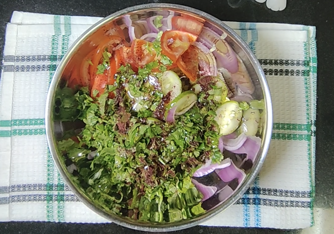 Sliced cucumber, tomato and red onion with chopped coriander, sumac and olive oil in a stainless steel mixing bowl