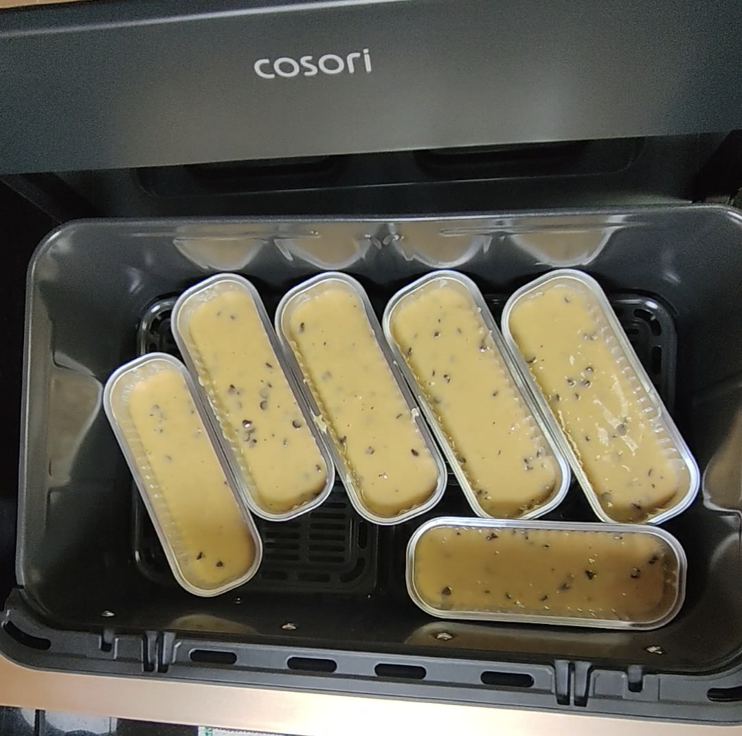 Six tins of uncooked chocolate chip batter arranged in a COSORI air fryer drawer