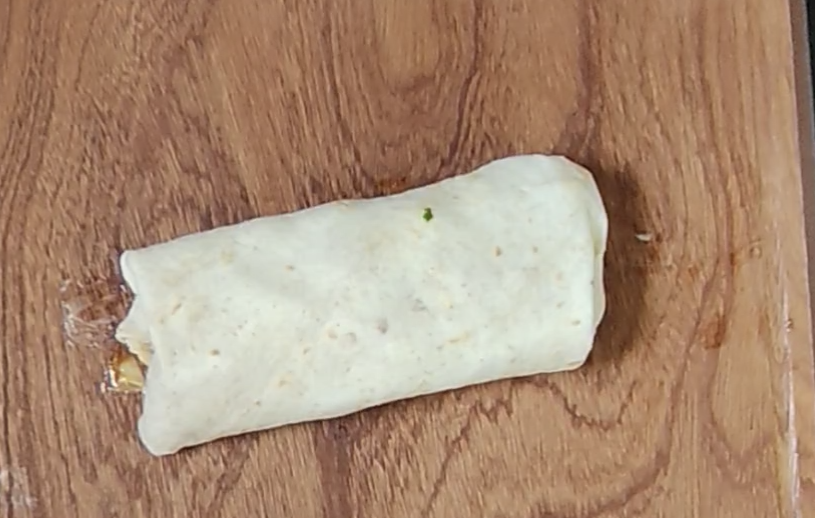 A folded chicken fajita wrap on a wooden board